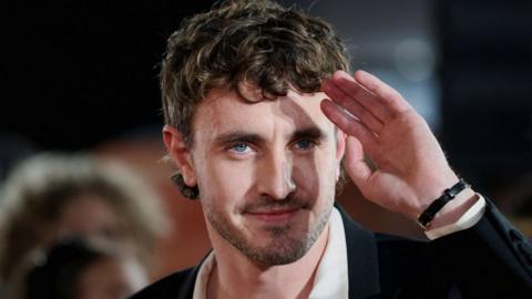 A close up of Paul Mescal's face as he holds up a hand to his forehead as he looks out to the crowd from the red carpet at the Gladiator II premiere,