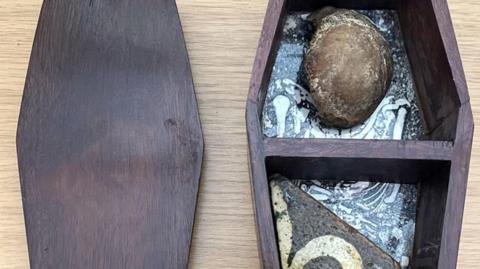 Image of a circular piece of knee bone and a section of tile in a small wooden box.