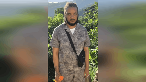 Keanu Taylor wearing a shirt and bag in front of plants. 