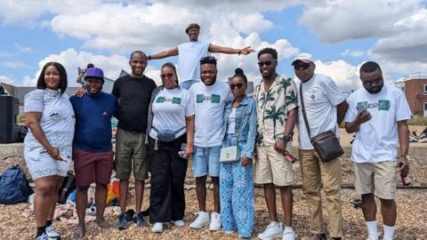 A large group of people stand in a line and smile at the camera on Felixstowe Beach.