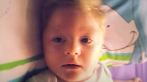 Charlie Cookson, a very young boy with short blond hair, lies on a bed