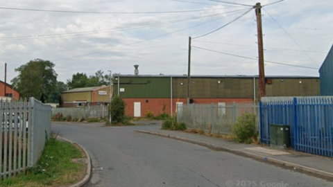 An industrial estate with metal fences and a narrow road
