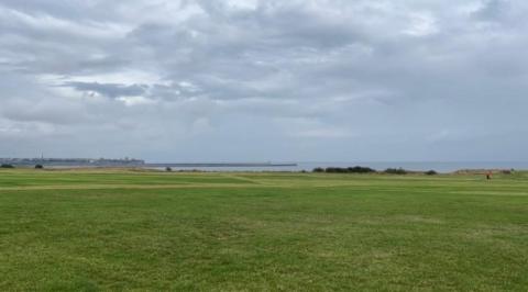 The Leas, along the coast road at South Shields. A grassy area lies in the foreground, with the sea in the distance and grey, stormy skies above.
