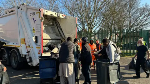 Several people take their bins to the back of a bin lorry