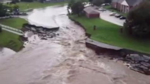 A road can be seen broken up, with brown water flowing through the centre of it.