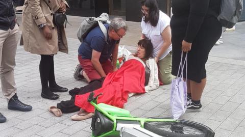 A woman is lying on the ground covered in a red blanket. A lime bike is on its side in front of her.