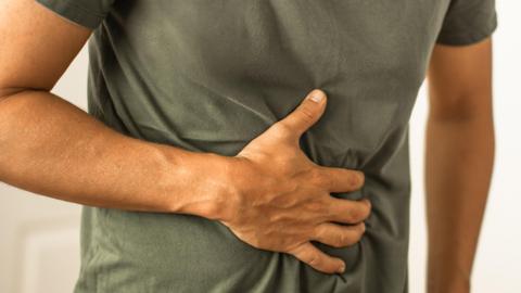 A man is clenching his stomach with one hand. He is wearing a khaki green T-shirt. 