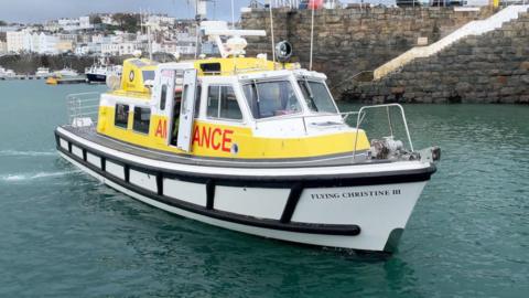 A white and yellow ambulance boat pulls out of a granite harbour.