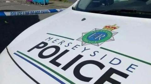 The bonnet of a Merseyside Police patrol car, with the force's badge and name painted onto a white background.