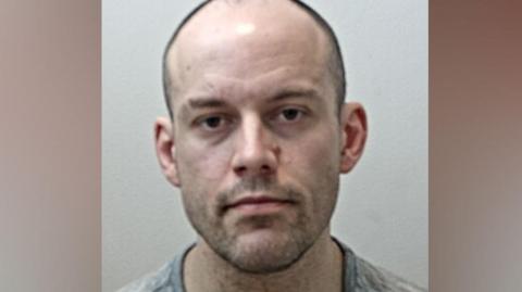 Matthew Matthiason's mugshot. He is balding with very short dark hair and stubble