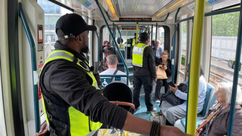 Security officers wearing high-visibility uniform on a packed tram in Nottinghamshire. 