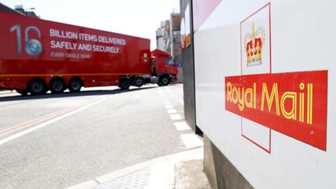 A white sign with a Royal Mail logo sits in the foreground. Behind it is a red Royal Mail delivery truck.