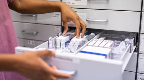 A close-up of a pharmacist searching for prescription medicine in storage rack