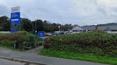 A street view image of a Tesco supermarket in Penzance. Hedges line the perimeter of the car park.