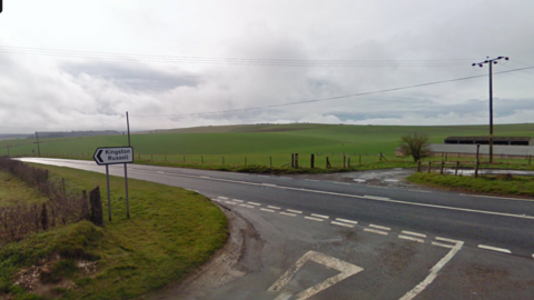 A Google Streeview image of the A35 running left to right, with green fields on the far side and a junction in the foreground