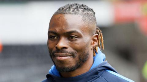 Former footballer Gabriel Zakuani - he has a short beard, braided hair and is wearing a blue hoodie. 