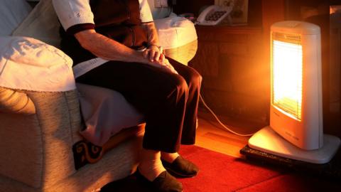 Generic stock photo of an unidentified elderly woman sitting at home in Liverpool with her electric halogen fire burning brightly in front of her.