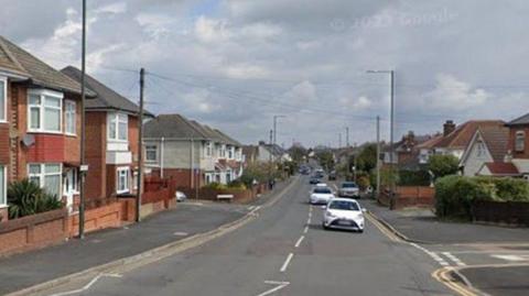 Kinson Road with homes lining both side and cars driving towards the camera. A junction can be seen on the right and then another further down on the left.
