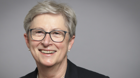 Baroness Gisela Stuart appears in a portrait photograph taken for her parliamentary office. She has short grey hair and thin framed glasses. She is smiling while wearing a pearl necklace and a black jacket.