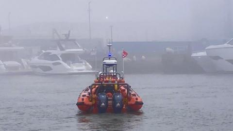 RNLI lifeboat seen from the rear on the water in foggy conditions with numerous boats.