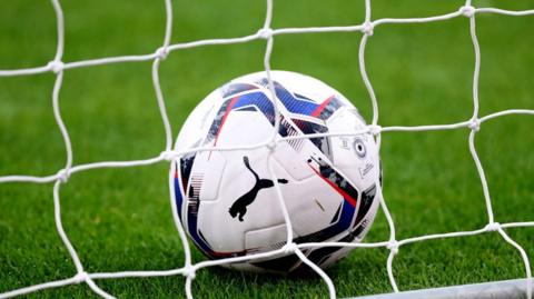 A white Puma football shown behind a goal net.
