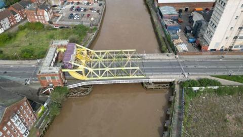 Aerial view of Drypool Bridge which has a yellow metal lifting mechanism and brick control room at one end spanning the roadway