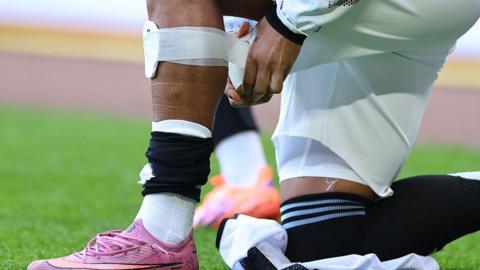 Jadon Sancho strapping a small shin pad on