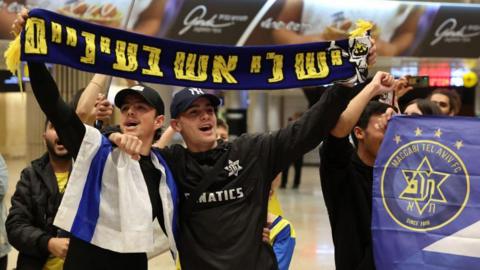 Maccabi Tel Aviv fans hold up a scarf in the airport before their trip to Amsterdam