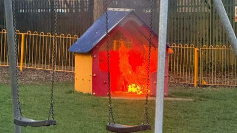A children's play area. There is a shed on fire.