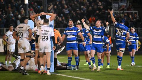 Exeter players (left) stand behind the post with hands on hips and arms on heads as Bath players (right) cheer and hold arms up in celebration at full-time