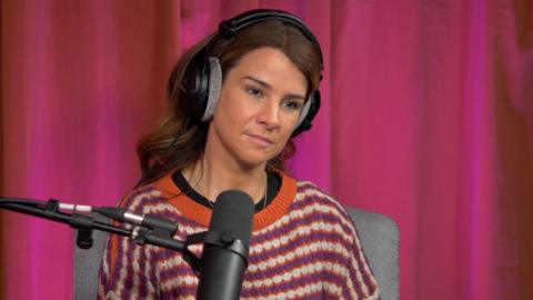 Izzy Judd, wearing a striped jumper and headphones, sitting behind a microphone