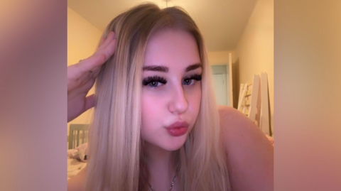 Tiffany, is a blonde woman in her late teens. She has thick dark eyelashes and pouts in this selfie.