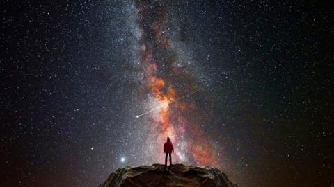 Image of person standing on a rocky surface surrounded by a dramatic starry sky