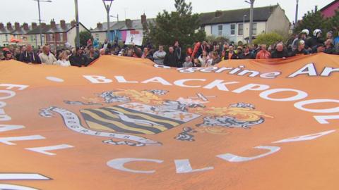 Protesting fans hold up a giant Blackpool club flag near the club's Bloomfield Road ground