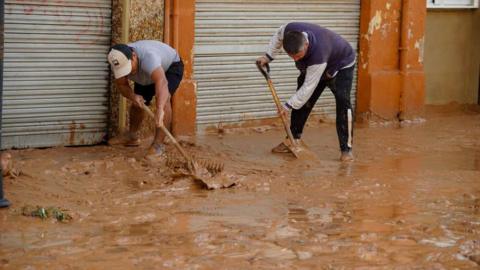 Residents in Valencia attempt to clear the road after flooding 