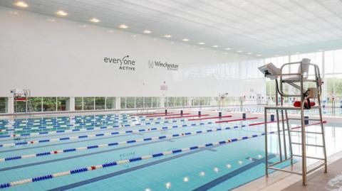 Swimming pool with lane ropes running along its length and a lifeguard seat on the near side of the pool.