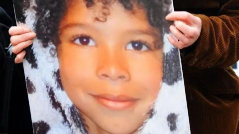 Hands holding a poster of a close up of the face of Zane Gbangbola aged seven