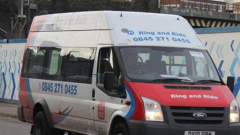 A white Ford mini bus with a red bonnet and blue writing which says "Ring and Ride" and a telephone number. 