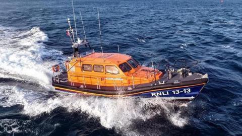 Swanage all-weather lifeboat in Swanage Bay. The sea is almost black with white waves surrounding the orange and navy blue lifeboat.