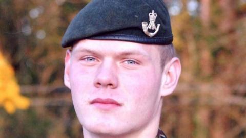 A young man with light blue eyes wear a tilted Army beret with a gold Army crest pin attached to the side.