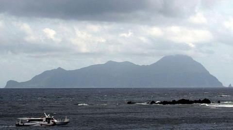 Akuseki Island, one of the main islands for tourists visiting Tokara, is seen in the horizon. A small ferry is in the sea, in the foreground