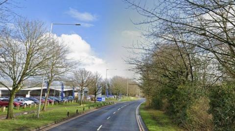A tree-lined road with a car showroom in the distance to the left