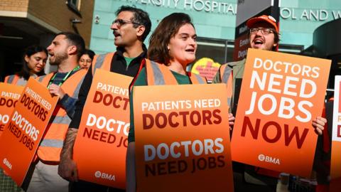 A group of resident doctors strike outside Bristol university hospital on Tuesday morning, they carry placards reading 'doctors need jobs now' and 'pay restoration for doctors'.