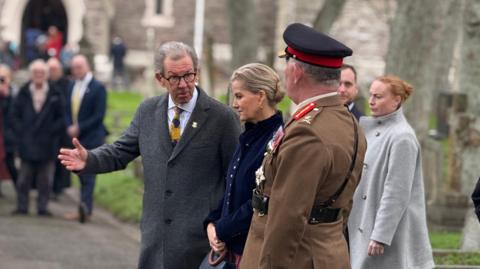 President of the States of Alderney William Tate talks to the Duchess of Edinburgh while walking outside a church.