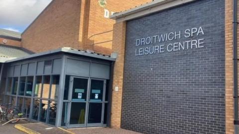 Droitwich Spa Leisure Centre which is a  red brick building, with grey reception area and silver lettering 