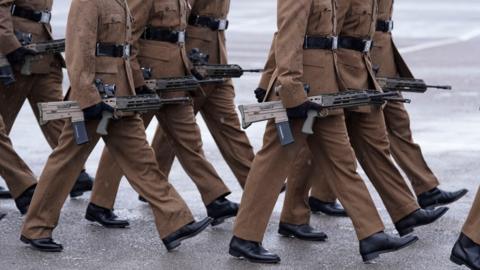 A shot of members of the armed forces marching and carrying rifles