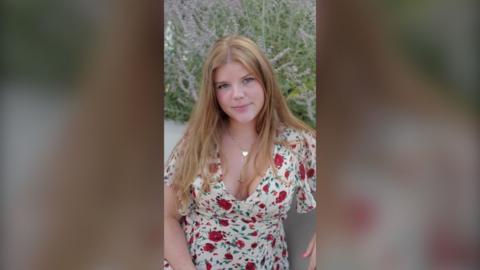 A young woman with long blonde hair wearing a flowery dress.