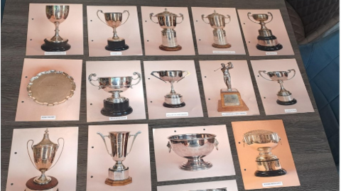 A series of photos of the trophies showing a range of silver shapes and sizes. the A4 prints are on a table.