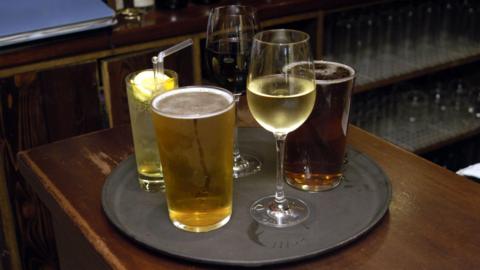 A selection of alcoholic drinks sit on a black tray on a pub bar.