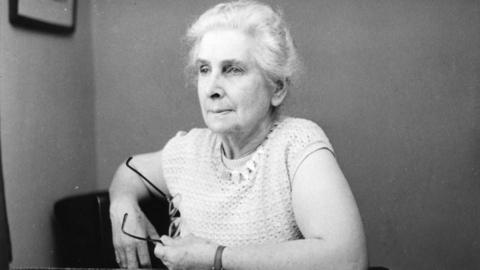 A black and white woman of a woman with light hair and a light top, holding some glasses